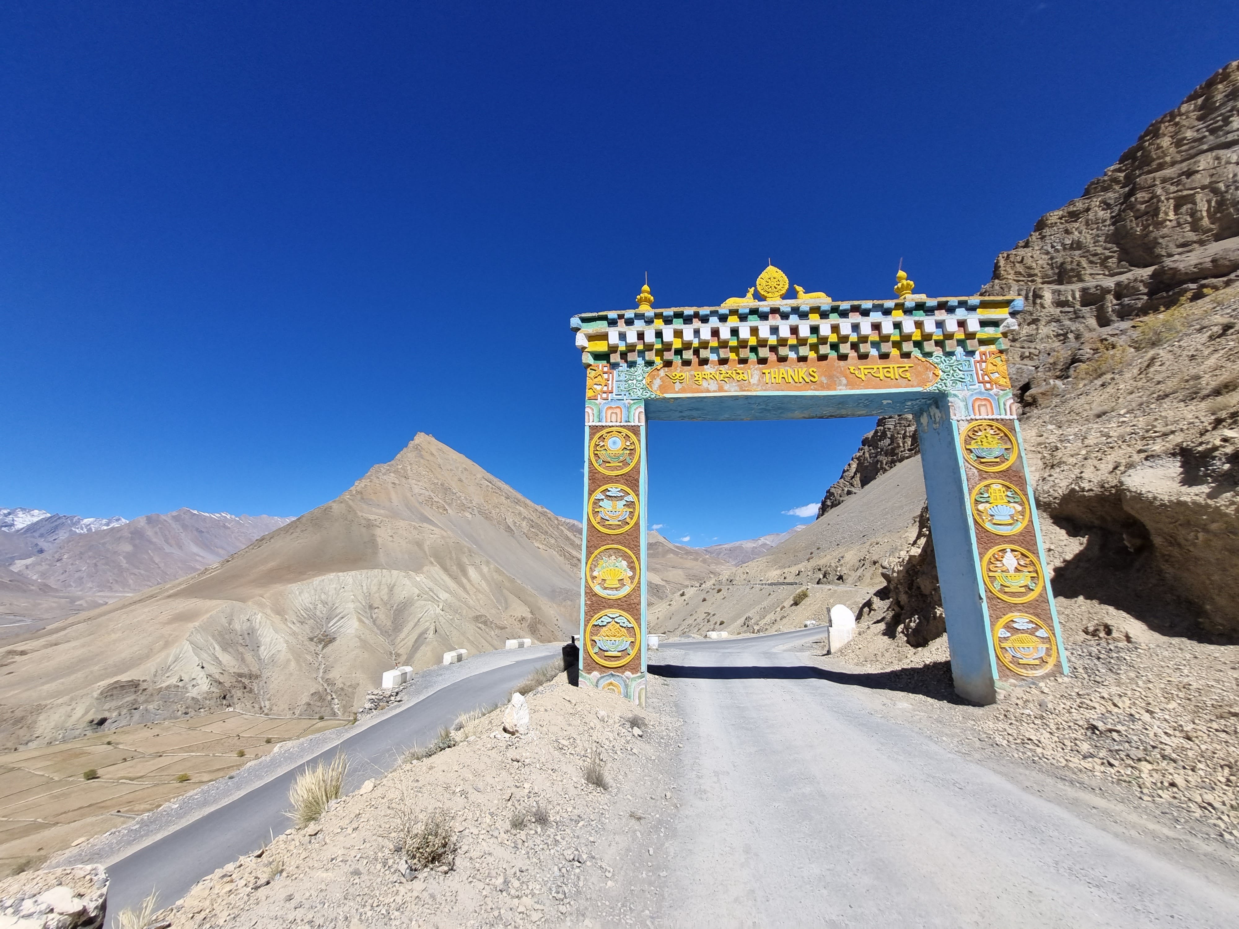 Hikers trekking on rugged mountain trail with snow-capped peaks in the background at Spiti Valley
